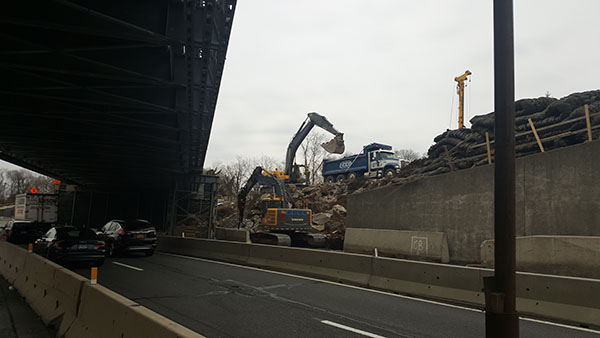 Volvo 235 with hydraulic hammer attachment breaks up blasted rock while a Volvo 460 loads it into a Mack tri-axle dump. 